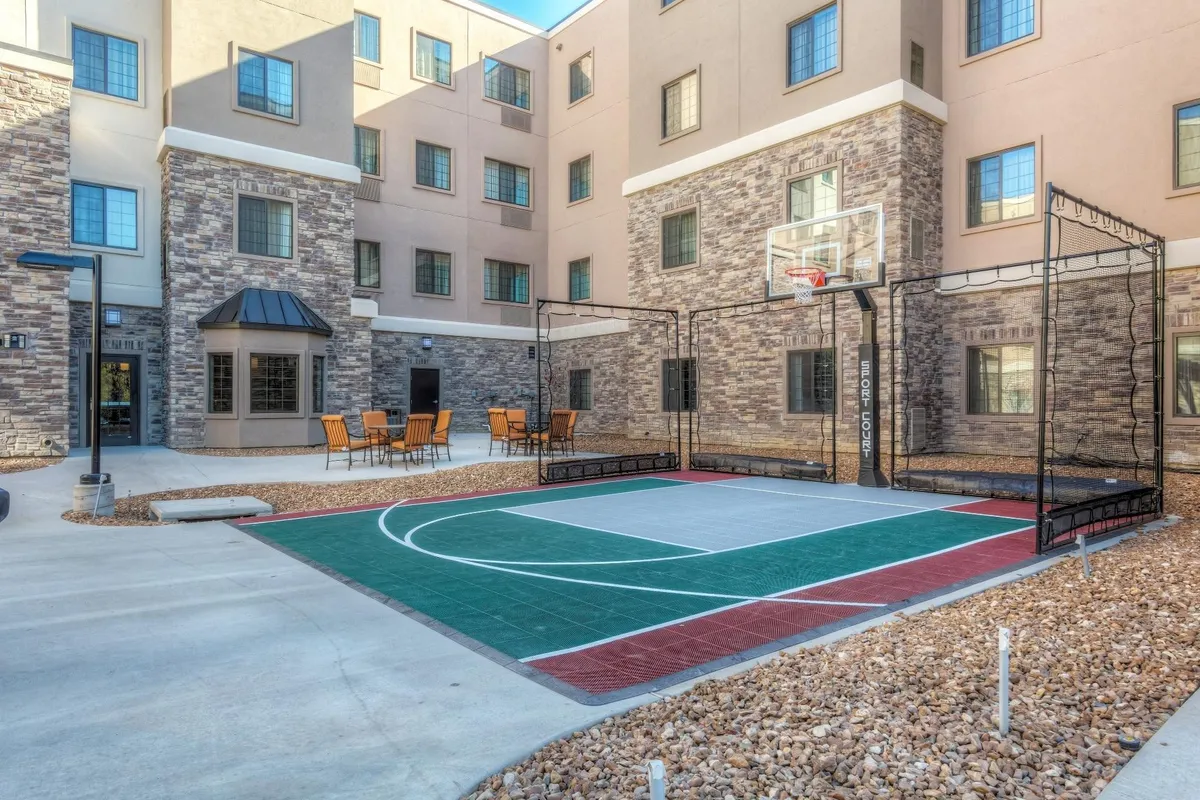 This exterior image features a vibrant basketball court adjacent to an outdoor seating area and the building's welcoming facade. The scene captures the energetic community spirit, with space for basketball games, relaxed gatherings, and family bonding. The outdoor setup hints at the property's proximity to parks and its suitability as a family-friendly launchpad for local adventures.