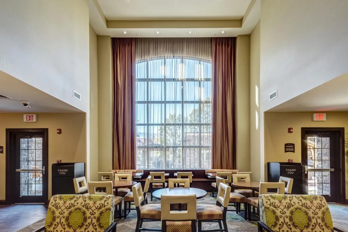 A spacious, inviting living area featuring a large arched window that fills the room with natural light. The comfortable seating arrangement and decorative patterned chairs evoke a welcoming, home-like atmosphere ideal for relaxation or informal gatherings.