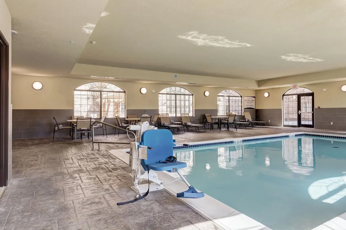 An inviting indoor pool scene, with a pool lift, lounge chairs, and sun-drenched large windows. The atmosphere is therapeutic and welcoming, perfect for families returning from a day out. The pool area offers opportunities for relaxation, swimming, and socializing, which aligns with the section’s mention of seasonal indoor pool amenities.